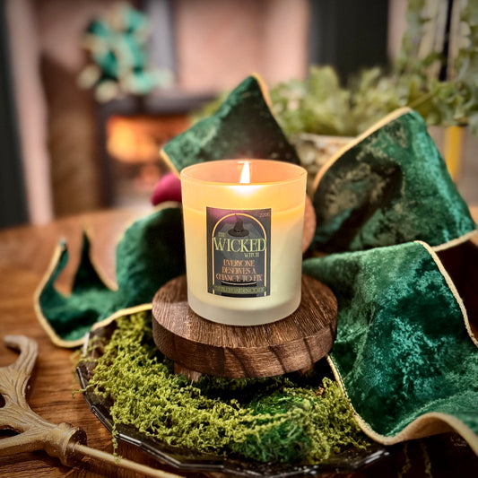 Candle with a label on a wooden stand surrounded by greenery and fabric