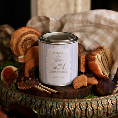 A tin of 'The Blue Garden' Crumbly Biscuit sits in an ornate decorative tray, surrounded by assorted cookies, a checkered cloth, and rustic wood elements.