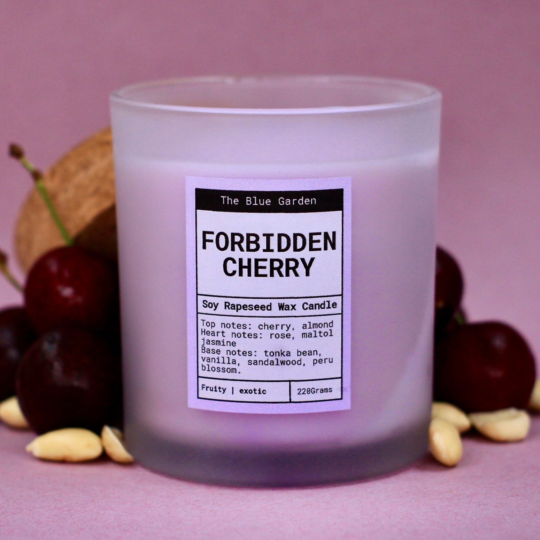 scented soy Candle labeled 'Forbidden Cherry' with cherries and almond nuts on a pink background. hand poured in Yorkshire by the blue garden