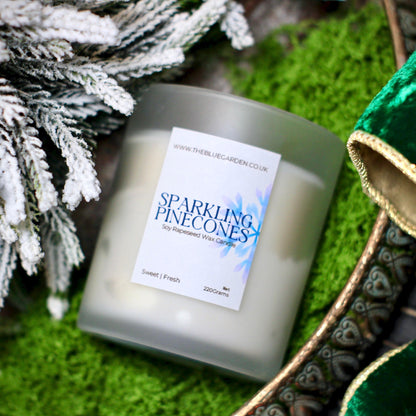 Candle labeled 'Sparkling Pinecones' with decorative elements on a green moss