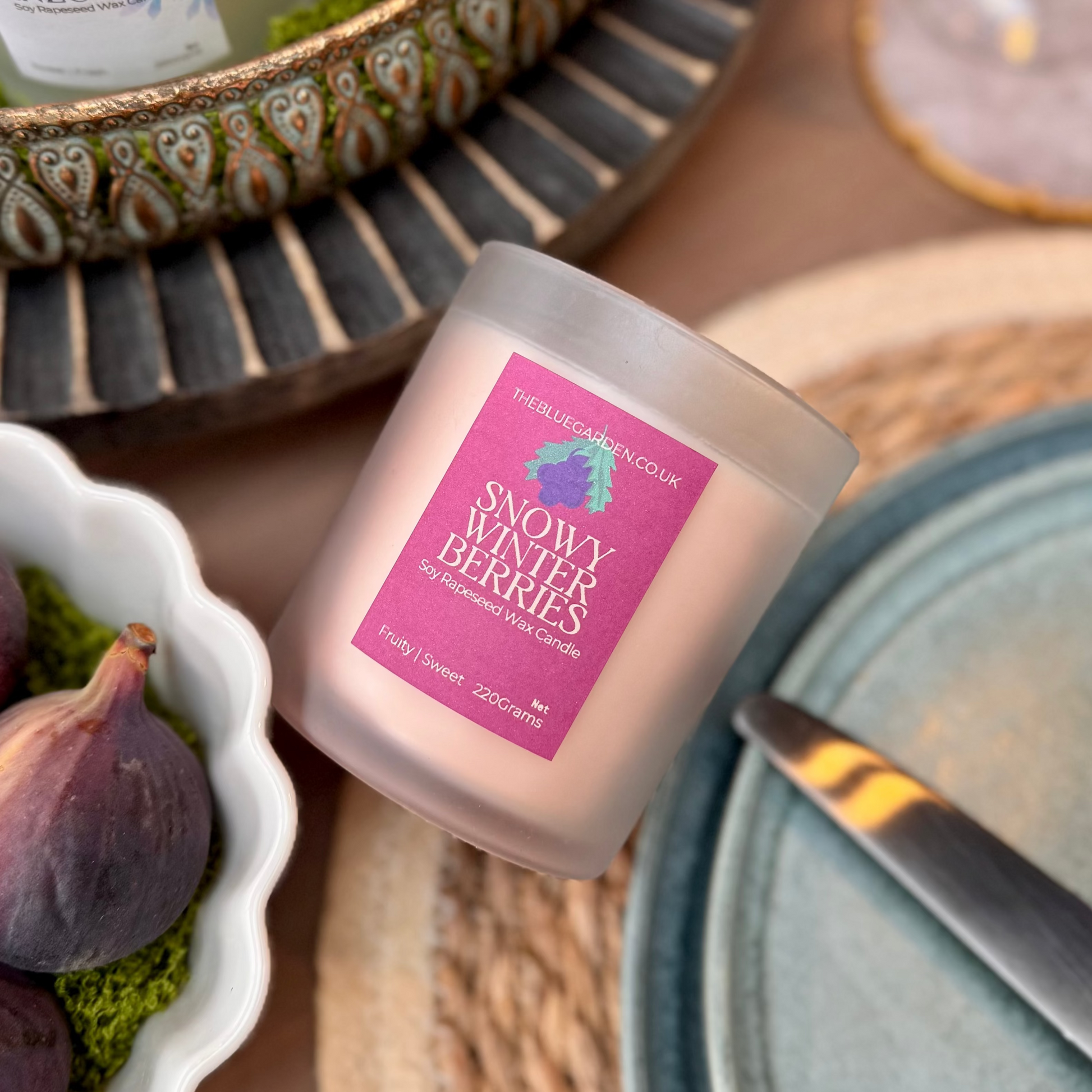 Winter soy candle with a pink label on a table setting with figs and cutlery