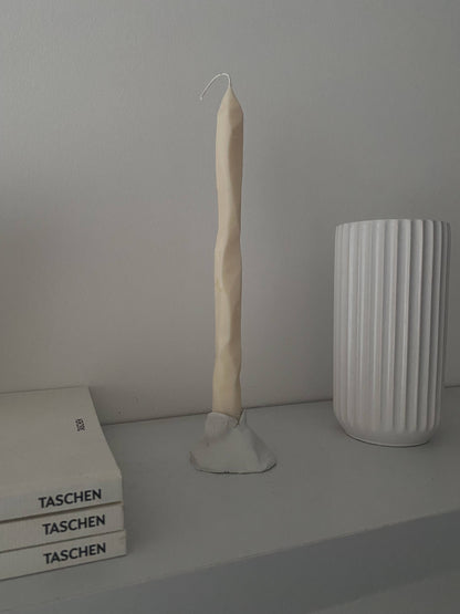 Wavy candle on a shelf with a white vase and 'Taschen' books in the background