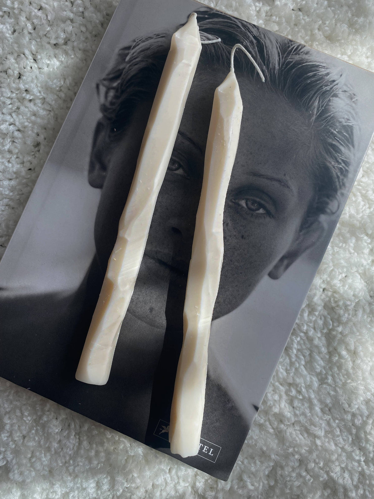 Two long, thin hand carved textural dinner candles on top of a magazine with a black and white photo of a woman's face.
