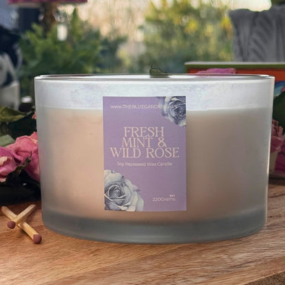 Candle with 'Fresh Mint & Wild Rose' label on a wooden surface outdoors