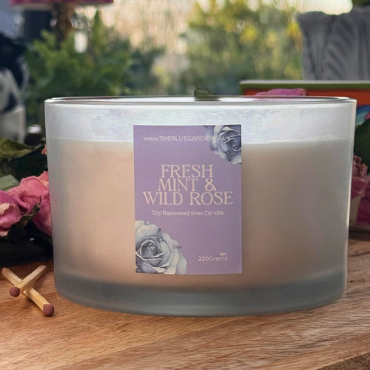 Candle with 'Fresh Mint & Wild Rose' label on a wooden surface outdoors